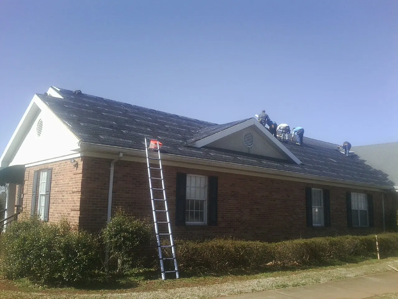 Crew tearing shingles off a brick ranch roof with a ladder set — Emergency Roof Repair work by our crew in Rock Hall