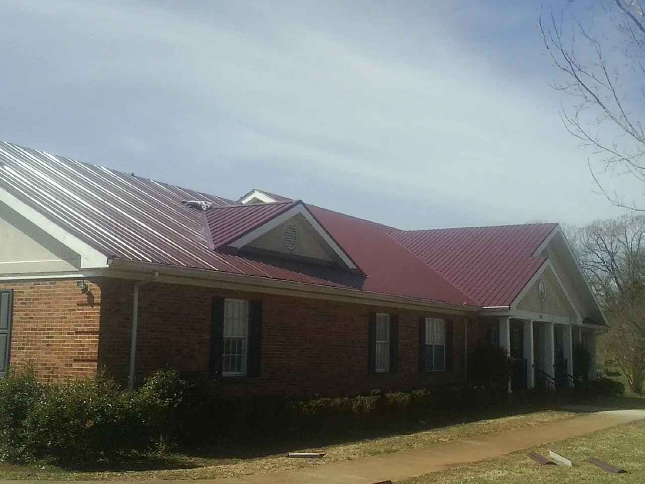 Red metal roof with gabled entries on a long brick building, from a Hail Damage Roof Repair job in Rock Hall