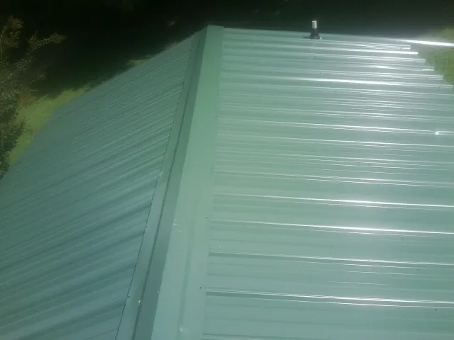 New green metal panels meeting at the ridge of a roof — Flat Roof Repair work by our crew in Rock Hall