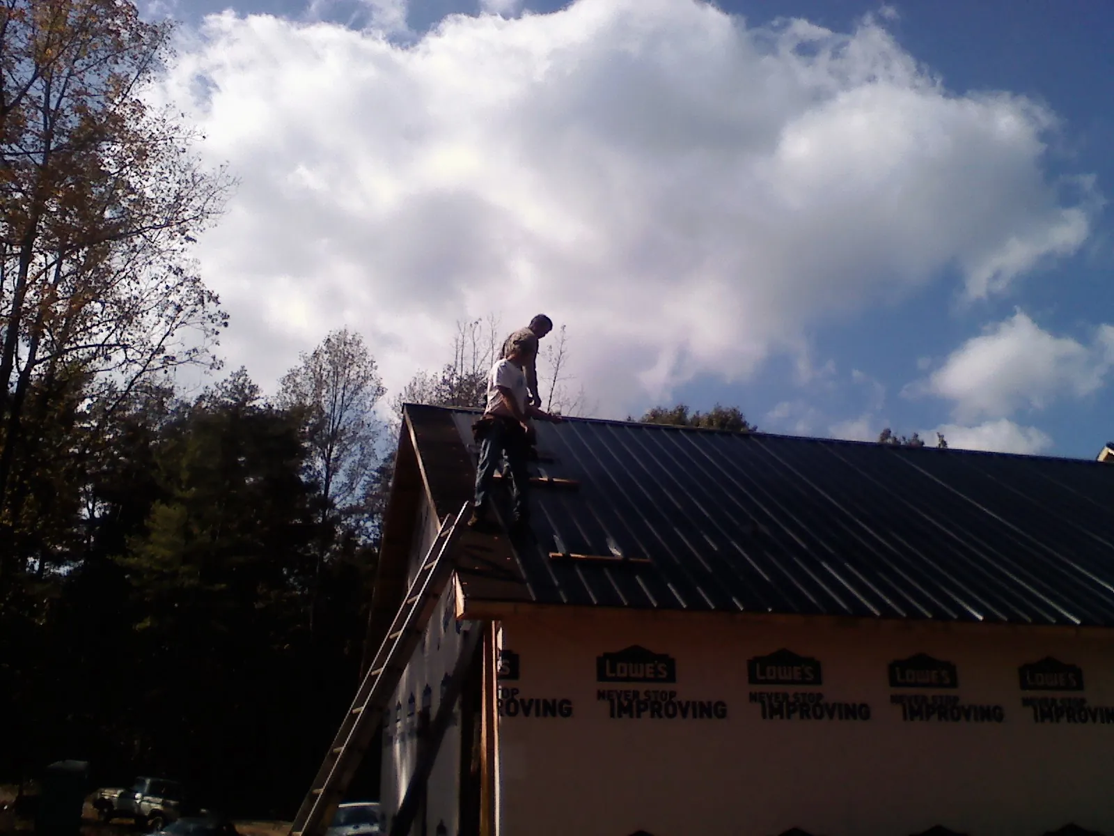 Roofer fastening dark metal panels high against a cloudy sky, from a Roof Inspection job in Rock Hall